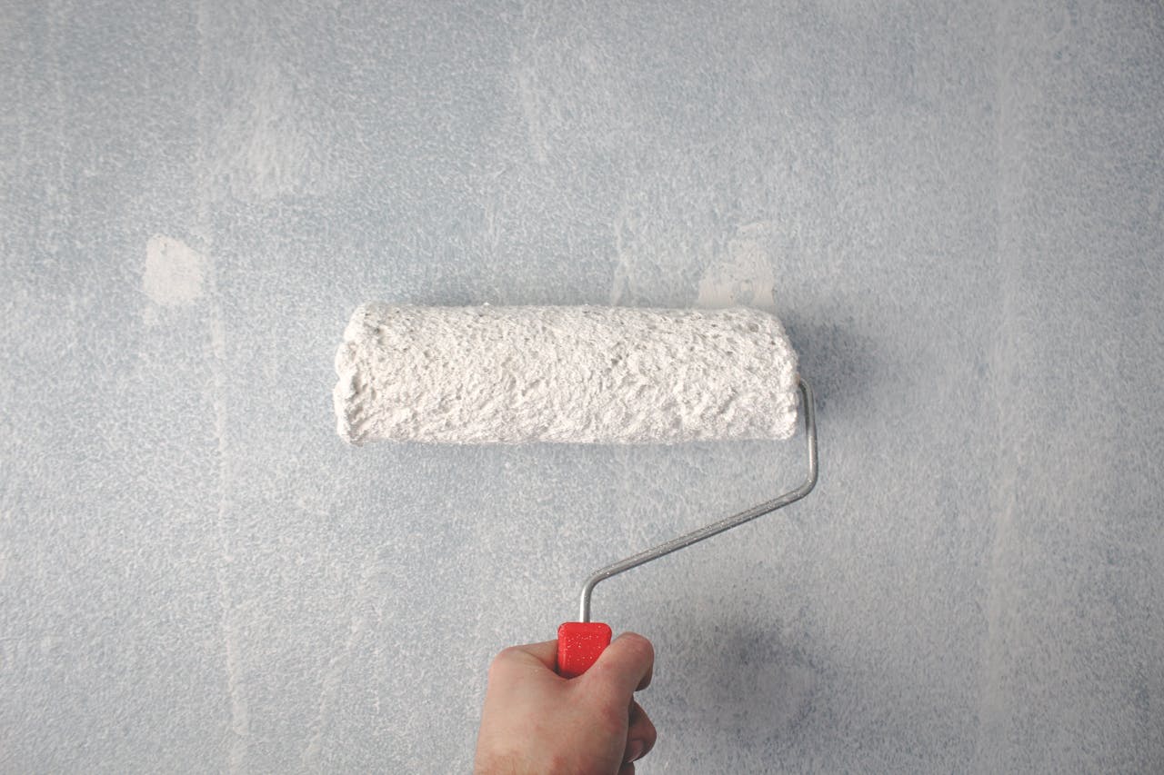 Hello world! A person's hand using a paint roller to apply white paint on a wall.